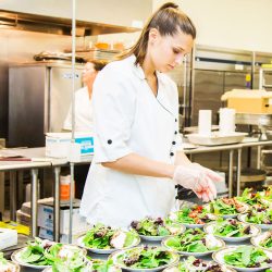 young woman with hair in a ponytail prepares salads for an event