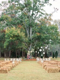 outdoor wedding ceremony space with big tree in back and hay seating